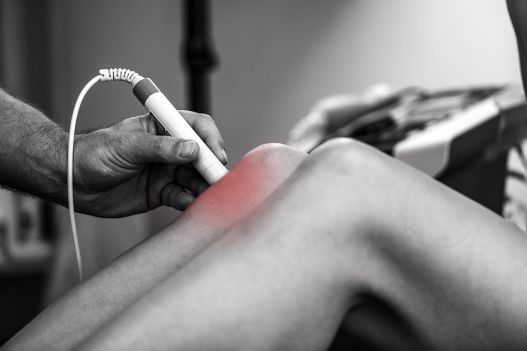 A physical therapist performs laser therapy on a patient's knee to reduce pain and inflammation, promoting faster recovery and improved mobility through targeted light treatment